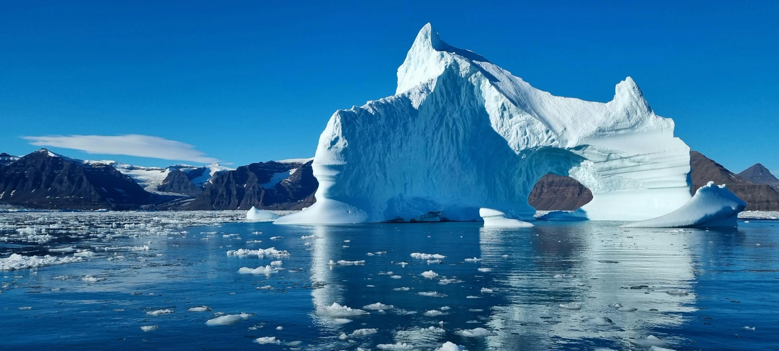 Iceberg on Body of Water Under Blue Sky